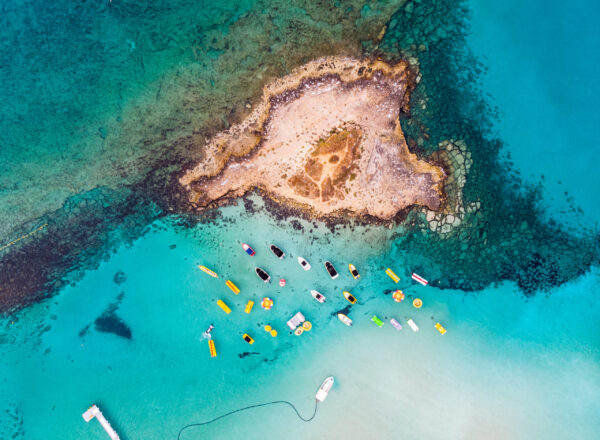 Island with boats parked near fig tree bay beach. Aerial vertical drone shot. Protaras, Cyprus